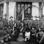 U.S. soldiers of Company C, 9th Infantry Regiment who survived a Filipino ambush in 1901 pose in Calbayog, Samar with a church bell used to signal the attack. The young boy, named Francesco, accompanied the men back to New York. The bells were taken as a war trophy to the United States.
